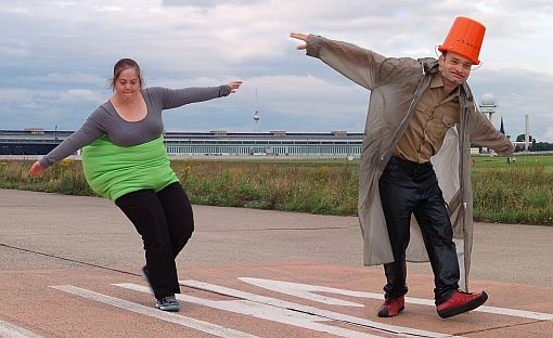 Foto: Pressefoto zum Stück "Wir werden gesehen" - Zwei Schauspieler bewegen sich in ihren Kostümen auf dem Tempelhofer Feld